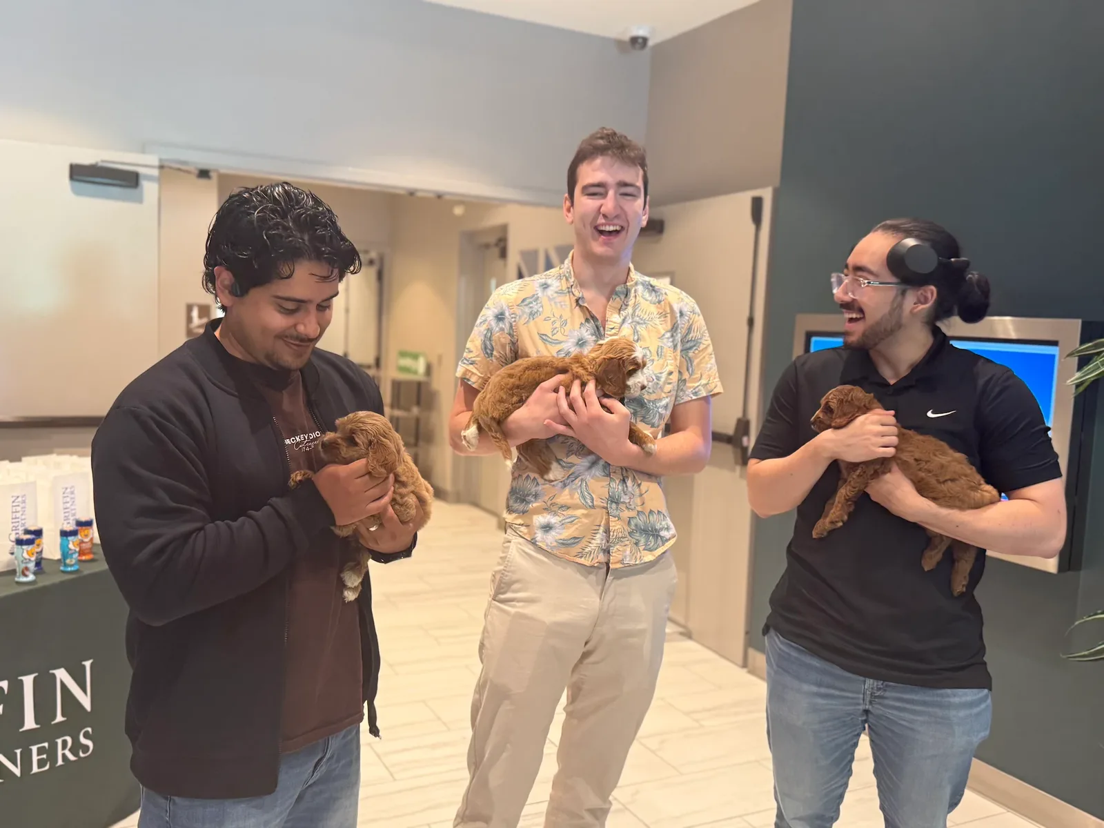 Three men with a puppy beside the Griffin Partners event signage